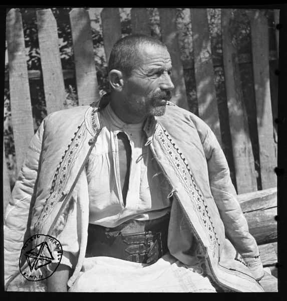 Țăran cu cojoc (BA-547) - Aurel Bau(c)h, 01 ian 1938 - 31 dec 1947 - Bărbat îmbrăcat în cămașă cu platcă din pânză țesută în casă, și cu chimir ciobănesc; pe deasupra poartă cojoc de blană, decorat cu fâșii subțiri de piele (irhă) și fir de lână colorată - foto preluat de pe www.facebook.com/@MuzeulTaranului